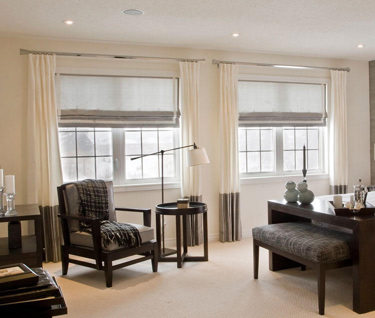 Cream banded drapes paired with gray Roman shades over two windows
