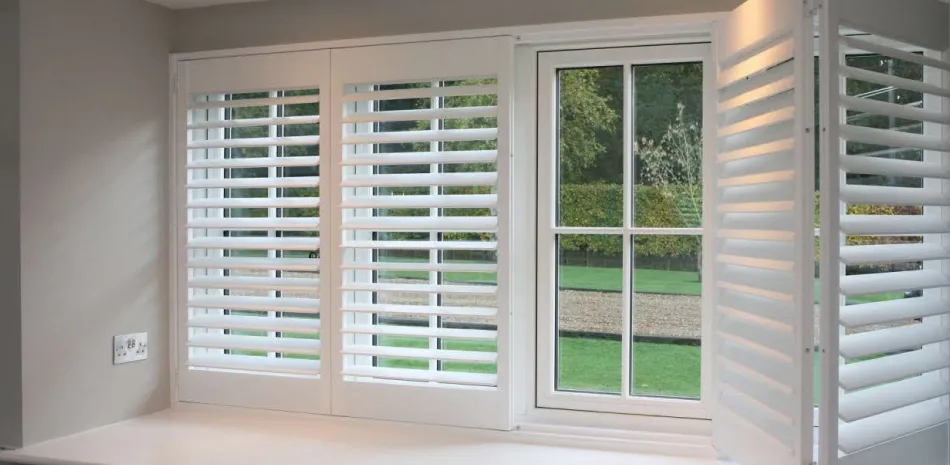 White plantation shutters in a bay window opening to a garden